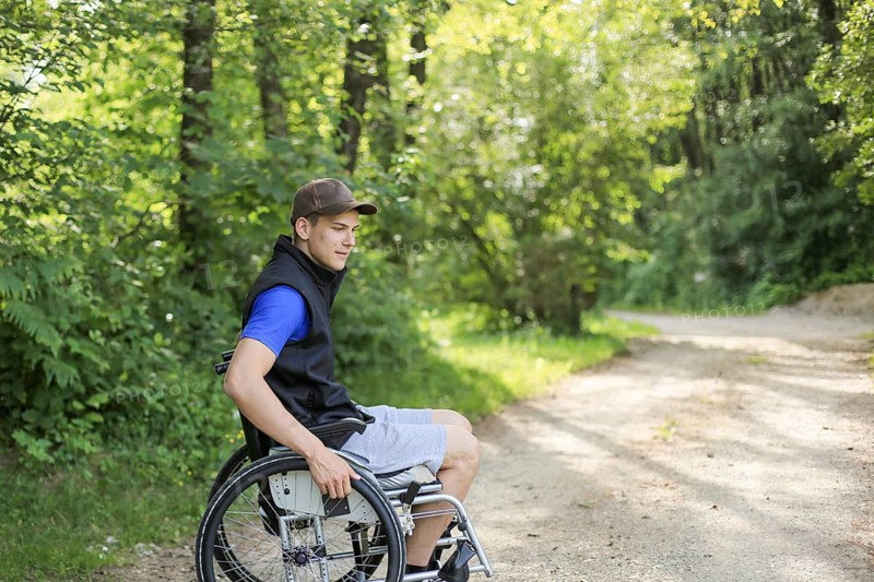 Happy and young disabled or handicapped man sitting on a wheelchair in nature turning wheels on a walking road at a beautiful sunny day