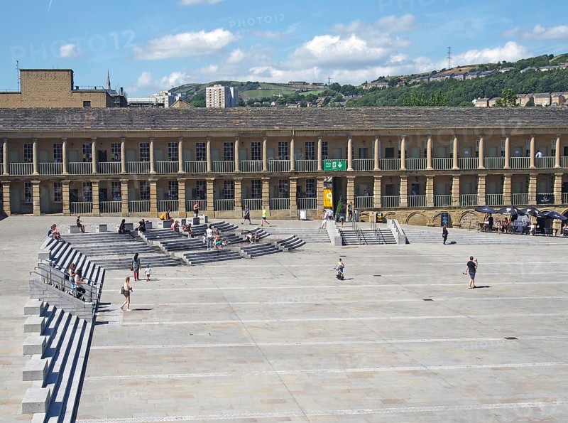 Halifax, west yorkshire, united kingdom, 23 july 2019: people relaxing on the steps and cafes and walking across the square of halifax piece hall in west yorkshire with a view of surrounding hills