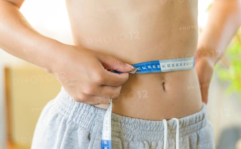 Skinny young woman measuring her slim waist with a measuring tape