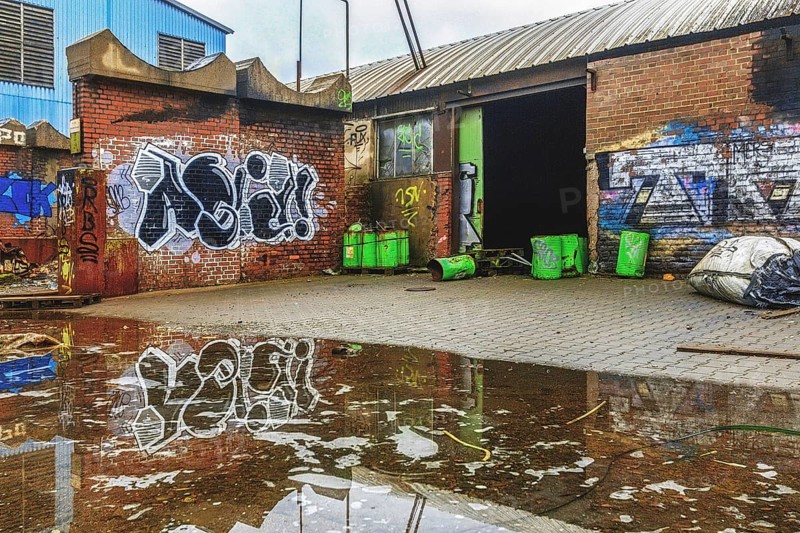 An abandoned courtyard with graffiti, puddles and green rubbish containers next to a brick wall, Metallwerke Bender, Lost Place, Linn, Krefeld, North Rhine-Westphalia, Germany, Europe