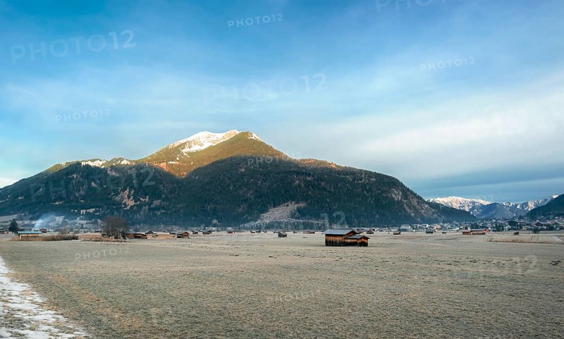 The Austrian Alps mountains, a village, and scattered barns on a meadow with frozen grass, near Ehrwald, Austria, in winter, Europe