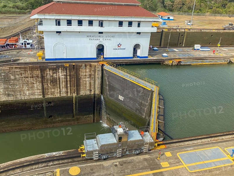 Lock with a locomotive on rails in front of a building. The canal is calm and the sky is clear, panama city, panamakanl, panama, Central America