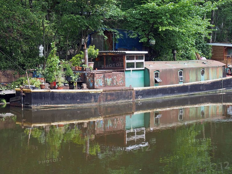 An old rusty narrow boat reflected in the water and surrounded by trees on the rochdale canal in hebden bridge west yorkshire