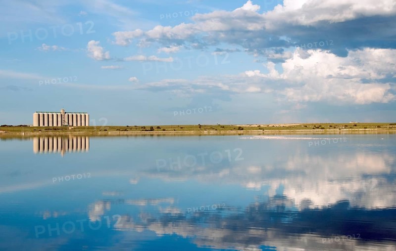 Corn Silos in South Africa, across a fresh water lake with blue skies and clouds, and a flock of pink flamingo in the water