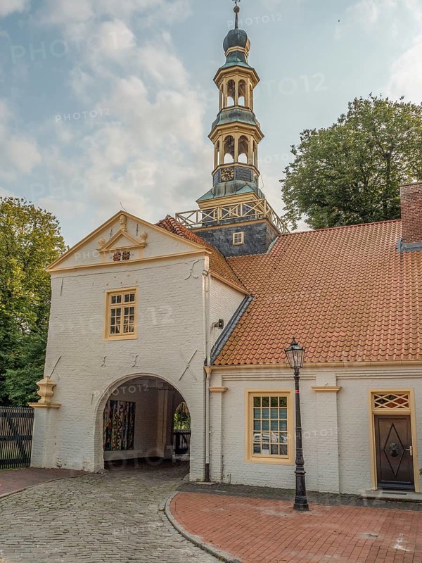 Historic building complex with archway entrance and a high church tower, with cobblestone path and lantern, dornum, east frisia, germany