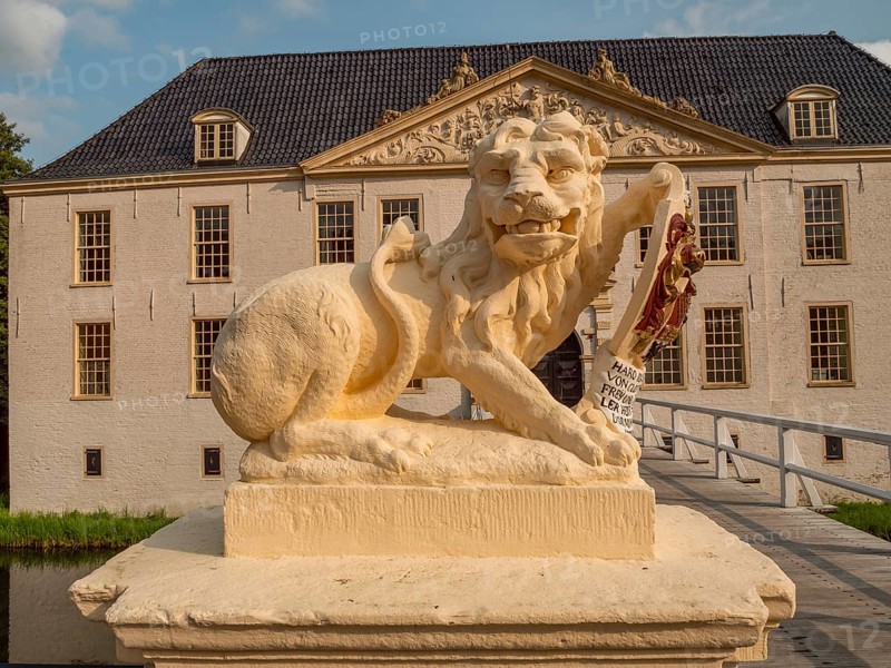Lion statue with coat of arms in front of a historic building and a bridge, dornum, east frisia, germany