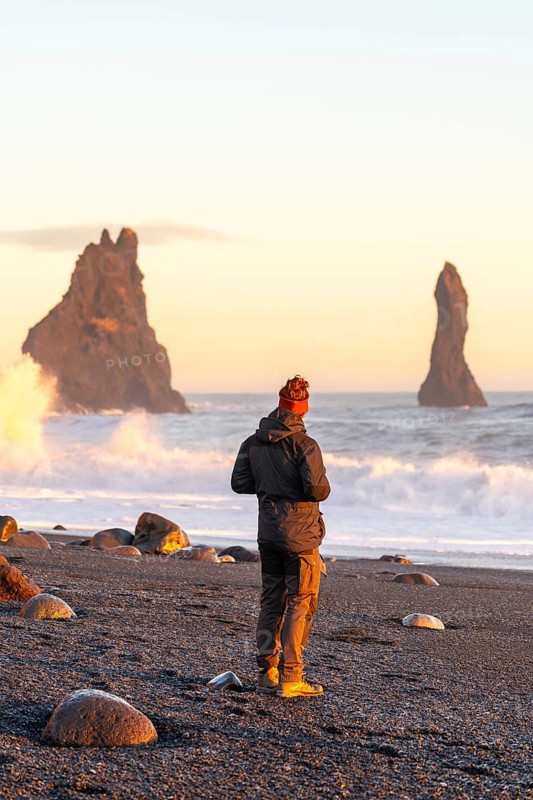 A tourist man with his back turned on the black sand beach of Reynisfjara at sunset in Iceland
