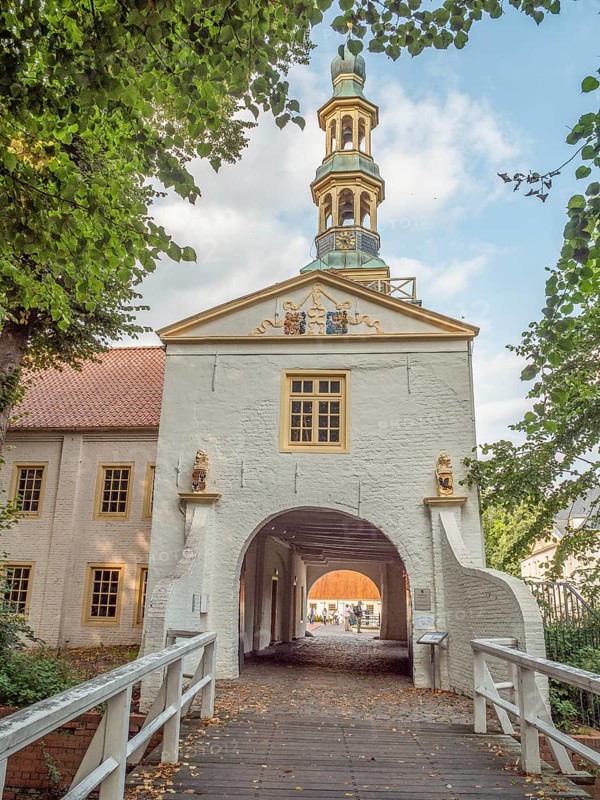 Tor tor with church tower above and decorative elements, offering a view of a building complex and a pedestrian bridge, dornum, east frisia, germany
