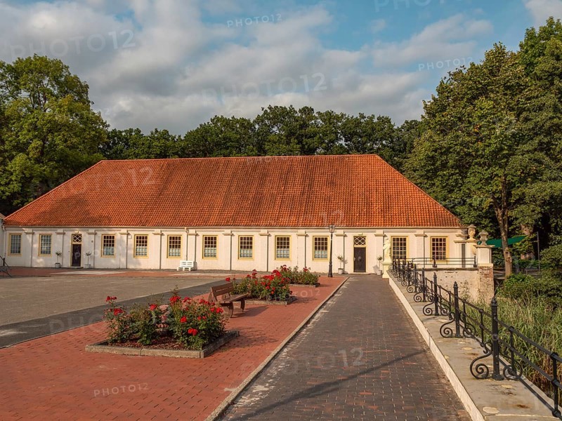 Courtyard with historic building, red roof and surrounded by trees with a flower bed, dornum, east frisia, germany