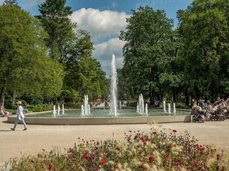 Central fountain in the park with walkers and lush greenery under a blue sky, Bad Lippspringe, Germany, Europe