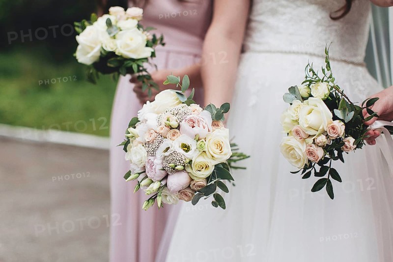 Bride in white dress is holding wedding bouquet with bridesmaids. Blurred background.