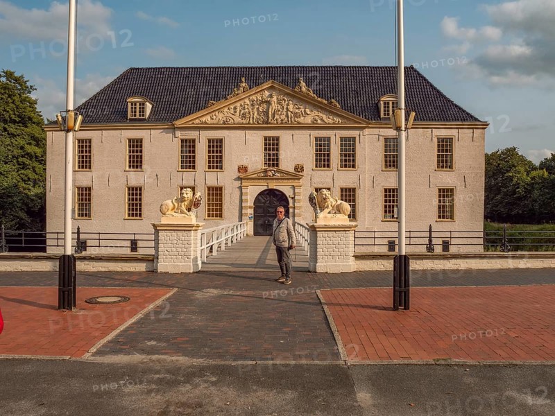 Man in front of a large historic manor house with lion statues and flagpoles in daylight, dornum, east frisia, germany