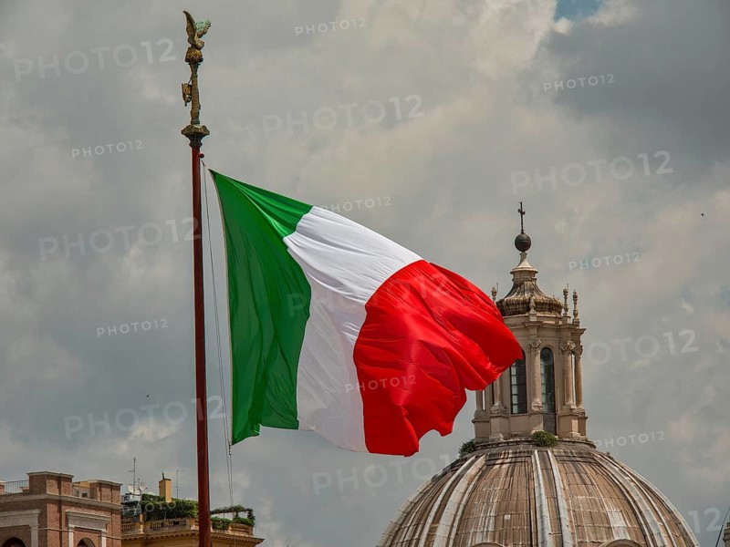 The Italian flag flies in front of a dome under a cloudy sky, rome, italy