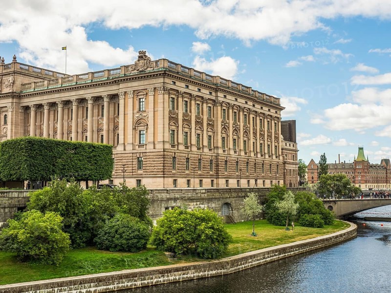 Impressive historic building on the canal with trees and bridge in the foreground under a partly cloudy sky, stockholm, baltic sea, sweden, scandinavia
