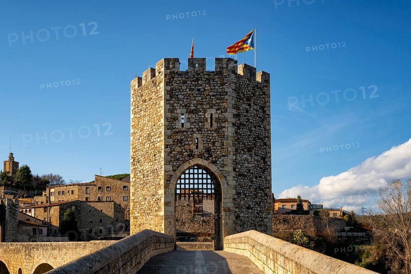 Besalu historic medieval city with Catalonia flags on the stone bridge tower crossing El Fluvia river, in Spain