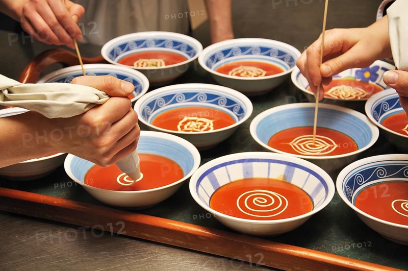 Busy cooks garnish bowls of tomato soup with fresh cream