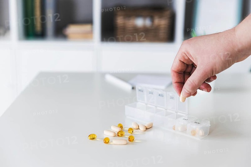 Closeup of female elderly hands sorting pills. Medical pill box with doses of tablets for daily take with white, yellow, beige drugs and capsules. Young woman getting her daily vitamins at home