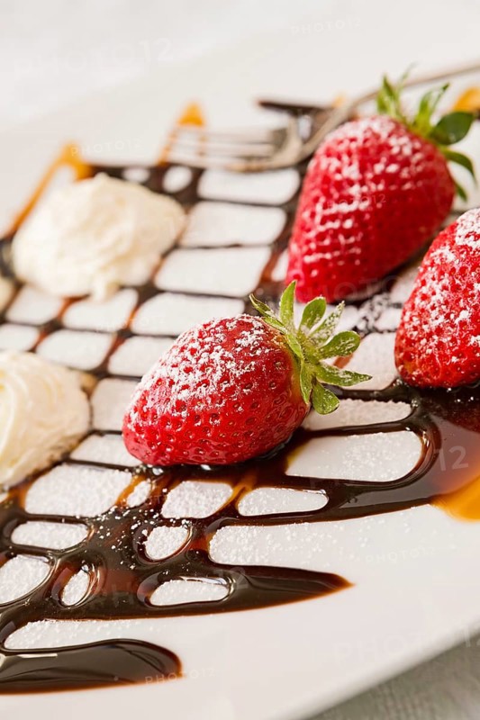 Close up of strawberries with whipped cream and decorations in a square plate