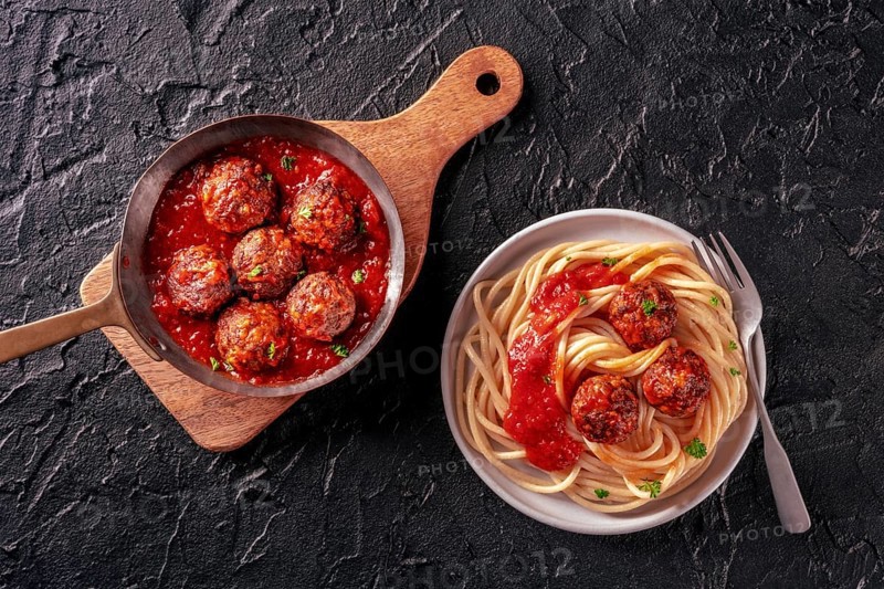 Meatballs. Beef meat balls, Italian dish, overhead flat lay shot in a pan and with a plate of spaghetti pasta, on a black background, Food photography