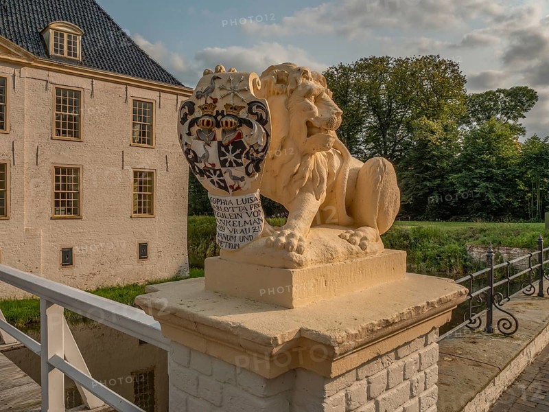Lion statue with coat of arms on bridge wall, buildings and nature in the background, dornum, east frisia, germany