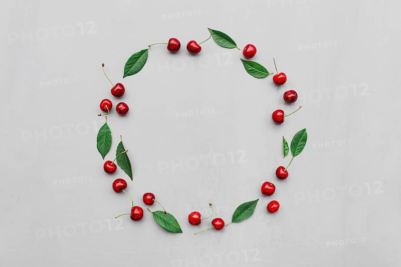 Gray concrete flat lay with big sweet cherries on table background. Top view on huge, massive organic cherry berries with leaves in form of empty circle shape. Copy space area for advertisement text