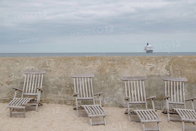 Abandoned deckchairs on the beach in front of a concrete wall with a cruise ship in the background, svaneke, bornholm, baltic sea, denmark, scandinavia