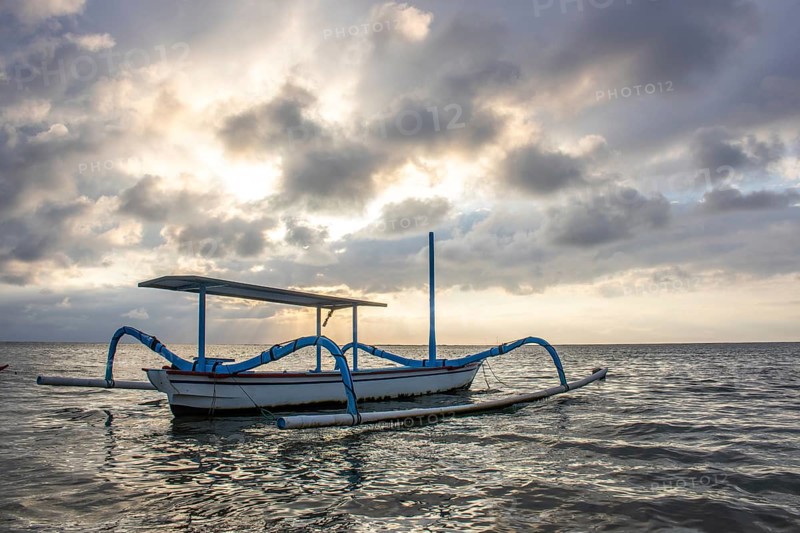 Jukung in the sea, typical landscape shot with a view of the horizon over the water, taken from a sandy beach. Traditional fishing boat at sunrise. Landscape shot of Sanur, Bali, Indonesia, Asia