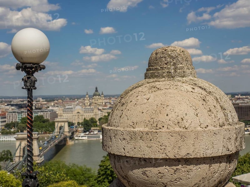 Stone ornament and street lamp with a view of the city and the river under a slightly cloudy sky, budapest, danube, hungary