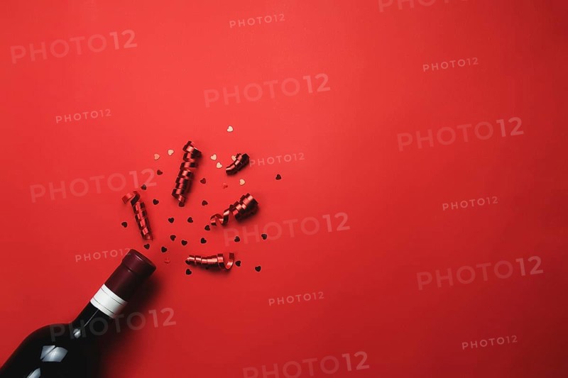 Valentine with bottle of wine, heart glitter and ribbon on red background.