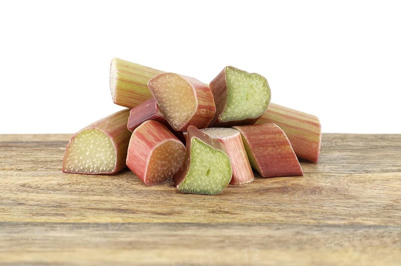 Variety of rhubarb stalks of varying colors from pale green to deep red on wooden cutting board isolated on white background