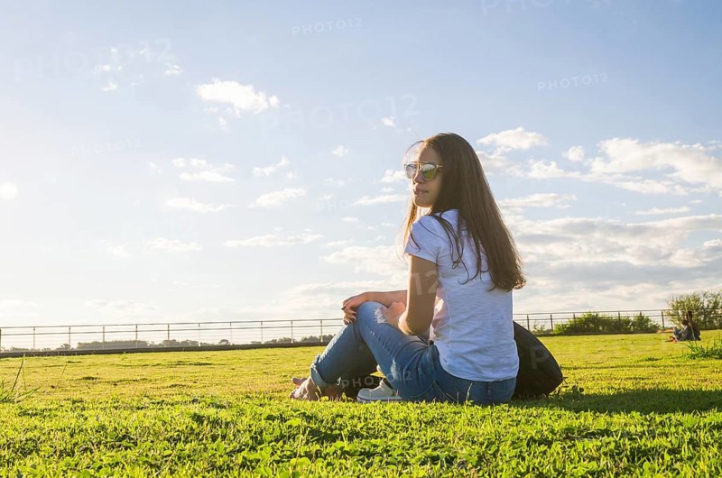Young woman sitting on the grass with a protective mask during the SARS CoV-2 pandemic season (COVID 19), on the new Orla do Guaiba in Porto Alegre on a beautiful sunset day