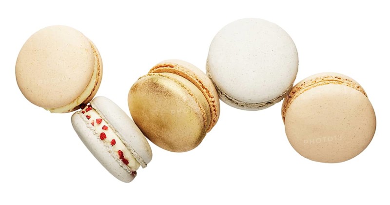 Isolated on white background white, yellow, gold macaron cookies flying, falling in motion or levitating. Colorful, sweet small French macaroon cakes. Five full cookies isolate.