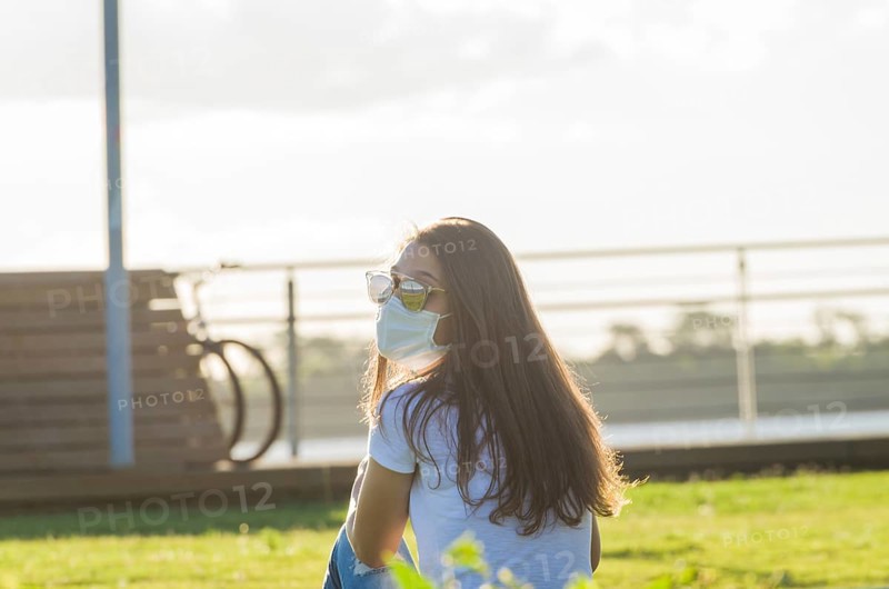 Young woman sitting on the grass with a protective mask during the SARS CoV-2 pandemic season (COVID 19), on the new Orla do Guaiba in Porto Alegre on a beautiful sunset day