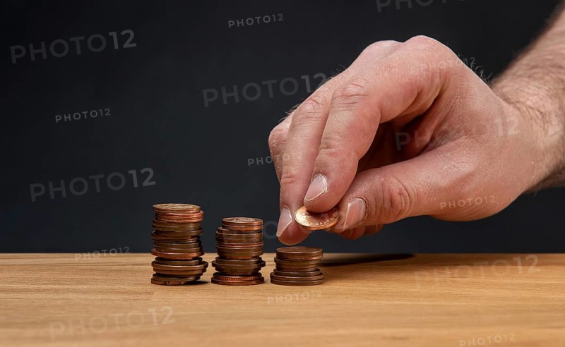 A hand stacking coins on a wooden table against a dark background