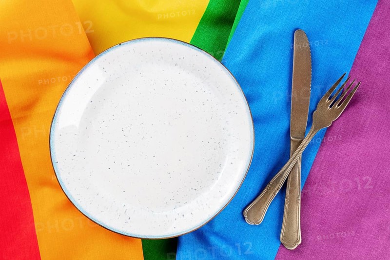 Gay food concept. A plate with cutlery, overhead flat lay shot on the LGBTQ rainbow flag texture, Food photography