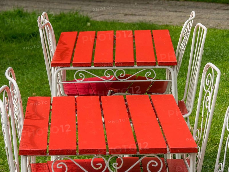 Two bright red garden tables with white metal chairs, decorated with artistic patterns, on a lush green lawn, ystad, sweden, baltic sea, scandinavia