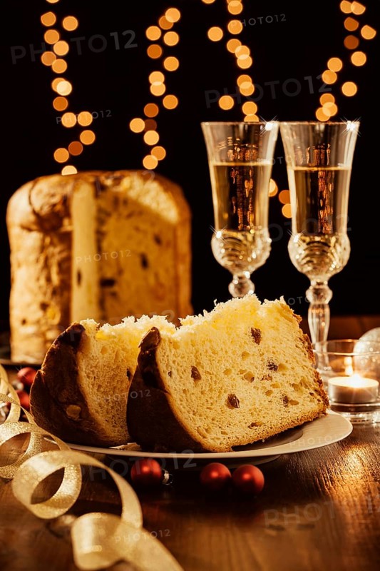 Sliced italian panettone, sparkling wine and decorations with Christmas lights on background
