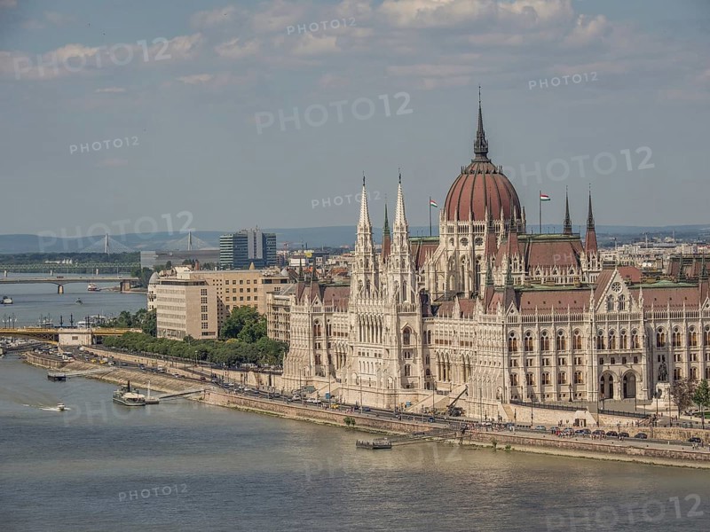 Large historic building on the riverbank with ships on the water and slightly cloudy sky, budapest, danube, hungary
