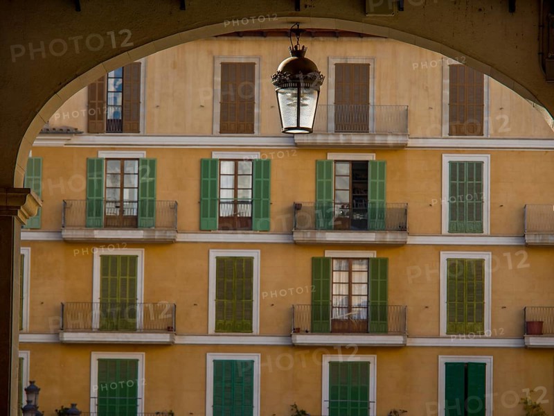 Yellow residential building with green shutters and balconies, framed by an arch with a hanging lantern, palma de Majorca, mallorca, balearic islands, spain