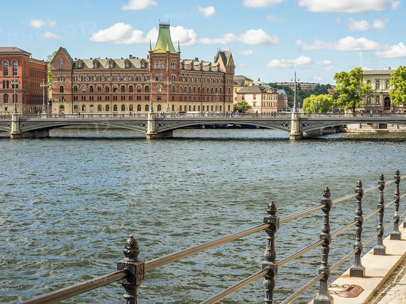 Riverside with a wrought iron railing, a bridge and historic buildings under a sunny sky, stockholm, baltic sea, sweden, scandinavia