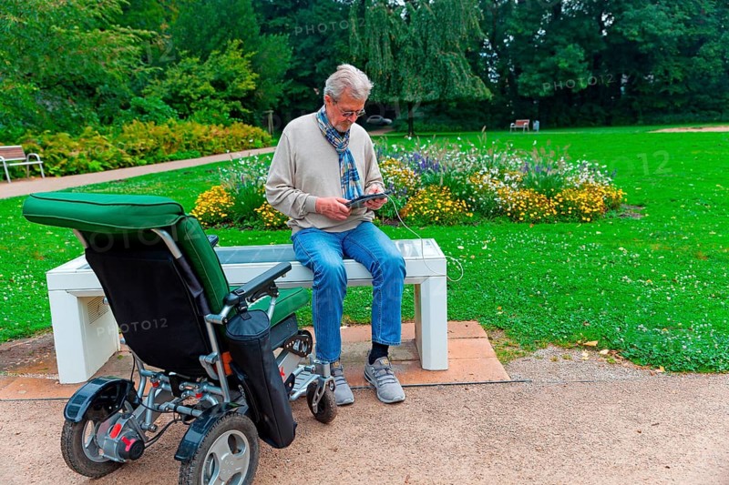 Man sits on a Smart Bensh and charges his Ipad, modern technology, bench with solar panel and charging option