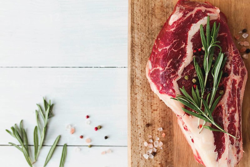 Raw ribeye steak on board, pepper, rosemary and pink Himalayan salt.