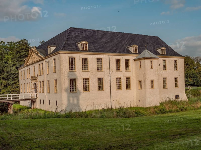 Historic castle with white walls and blue roof, nestled in a large green meadow under a blue sky, dornum, east frisia, germany