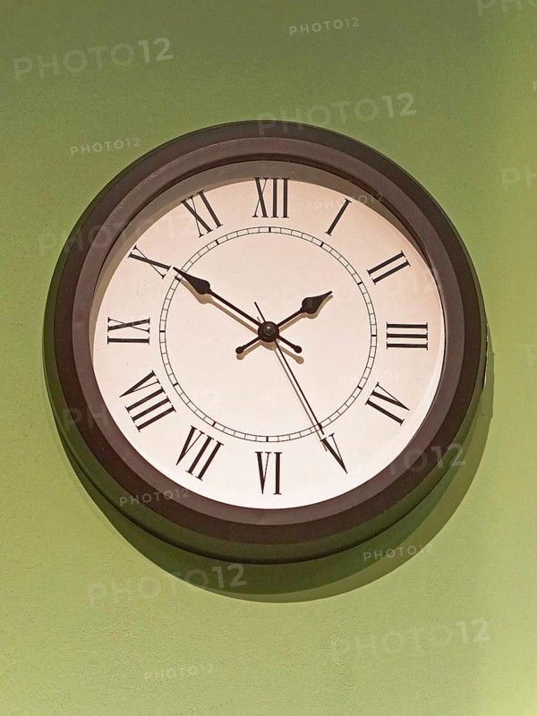 Big old clock with Roman numbers at green wall
