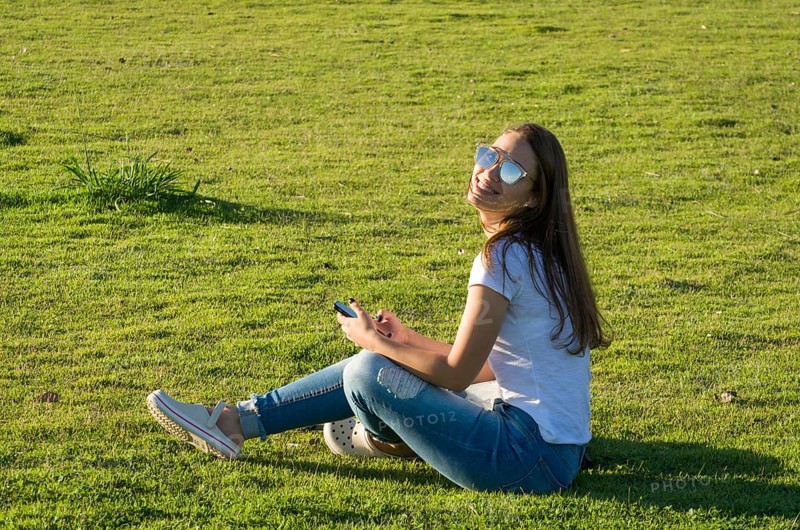 Young woman sitting on the grass, using smartphone on the new Orla do Guaiba in Porto Alegre on beautiful sunset day