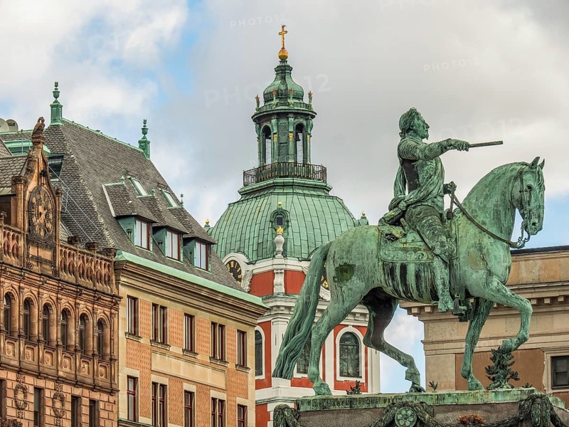 Bronze statue of a rider on a horse in front of a building with a central tower and clear sky, stockholm, baltic sea, sweden, scandinavia