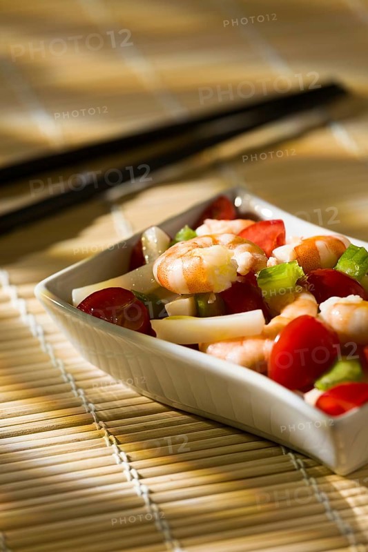 Shrimp salad with squid tomatoes celery inside a white bowl on a bamboo tablecloth and chopsticks