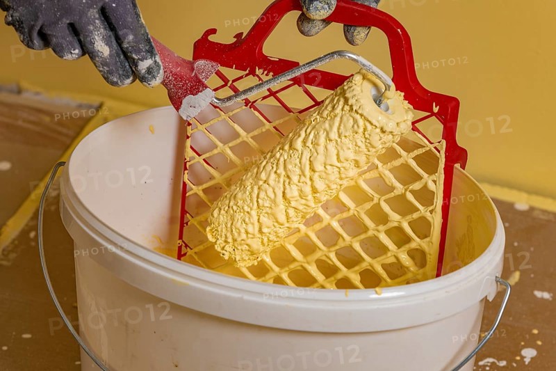 Paint roller on scraper grid in bucket with wall paint, painting work