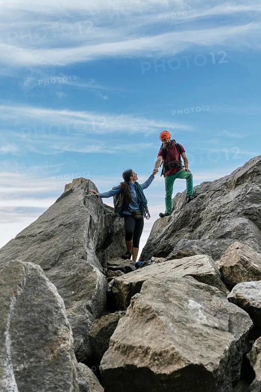 Male and female climbers high-fiving at the top of the mountain. Mixed rock climbing team
