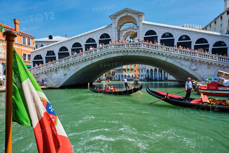 Italian maritime flag with Rialto bridge with boats and gondolas in the bacground. Grand Canal, Venice, Italy, Europe